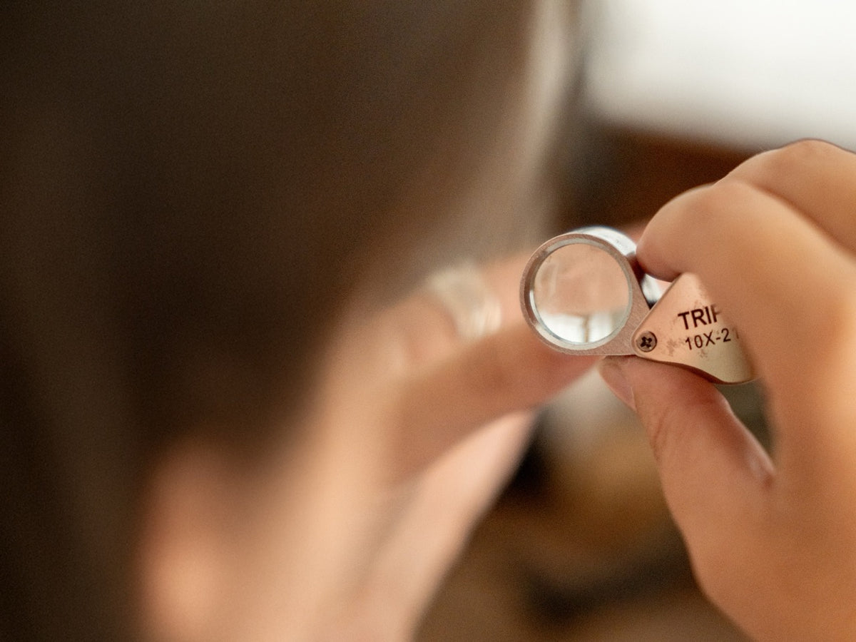 A close-up of a jeweller inspecting a piece through a magnifying loupe.