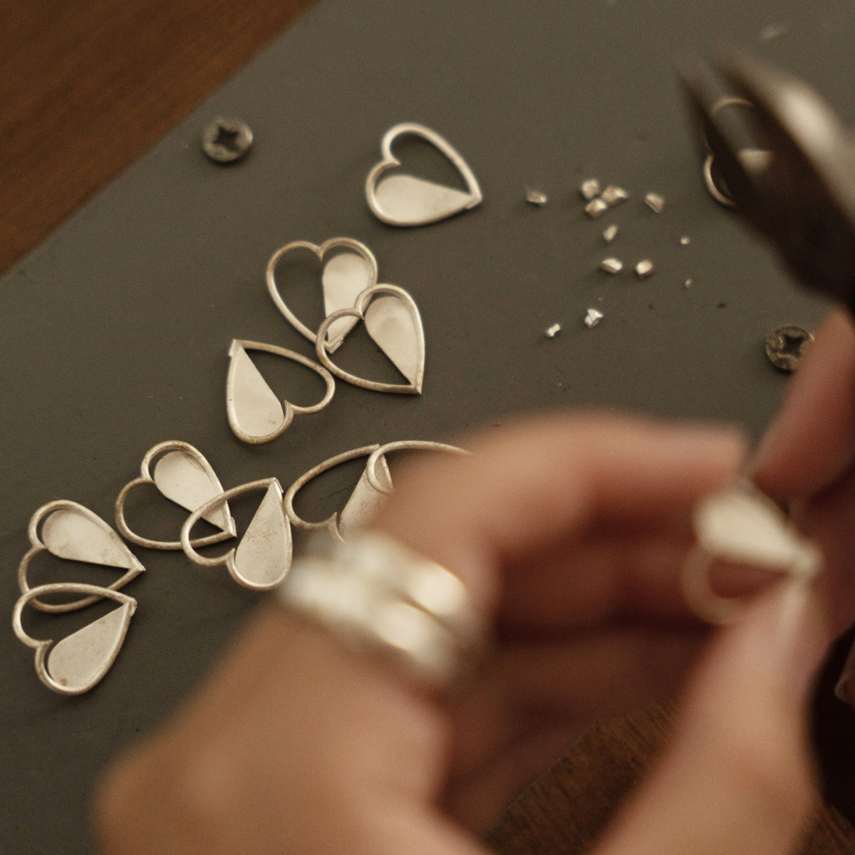 Hands working on heart-shaped jewellery pieces at the studio workbench.